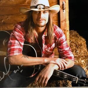 Man with guitar and cowboy hat sitting.