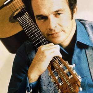 Man posing with guitar, wearing blue shirt.