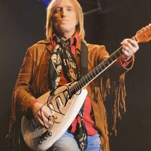 Musician playing guitar on stage, wearing fringe jacket.
