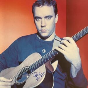 Musician playing acoustic guitar against red background.