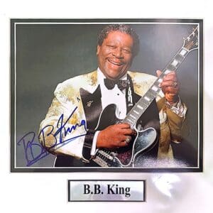 Smiling man with guitar and signed photograph.