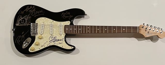 Black electric guitar with multiple signatures displayed.