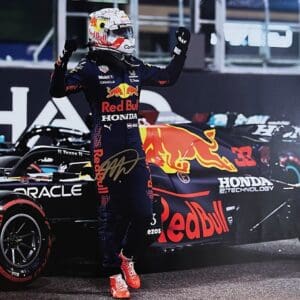 Race car driver celebrating beside Red Bull car.