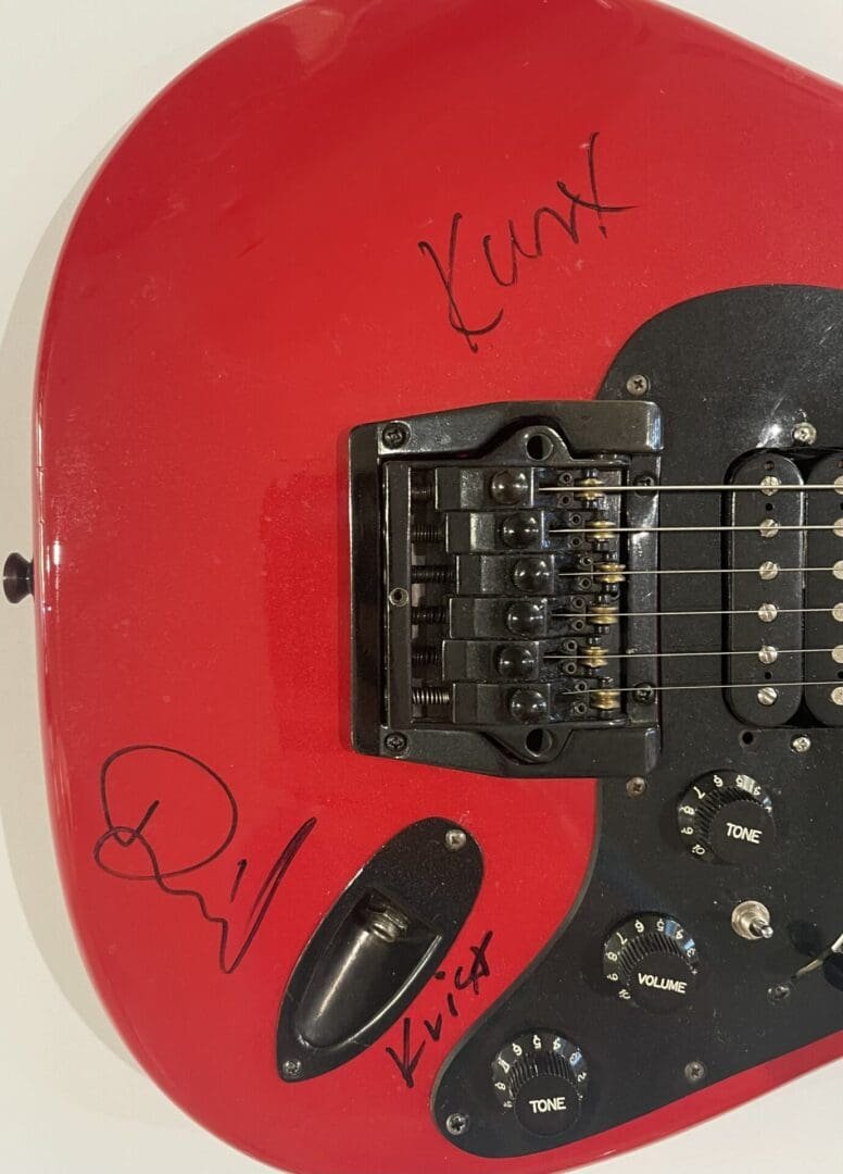 Red electric guitar with black signatures.