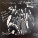 Rock band posing with autographs on album cover.