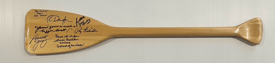 Wooden paddle with multiple signatures displayed horizontally.