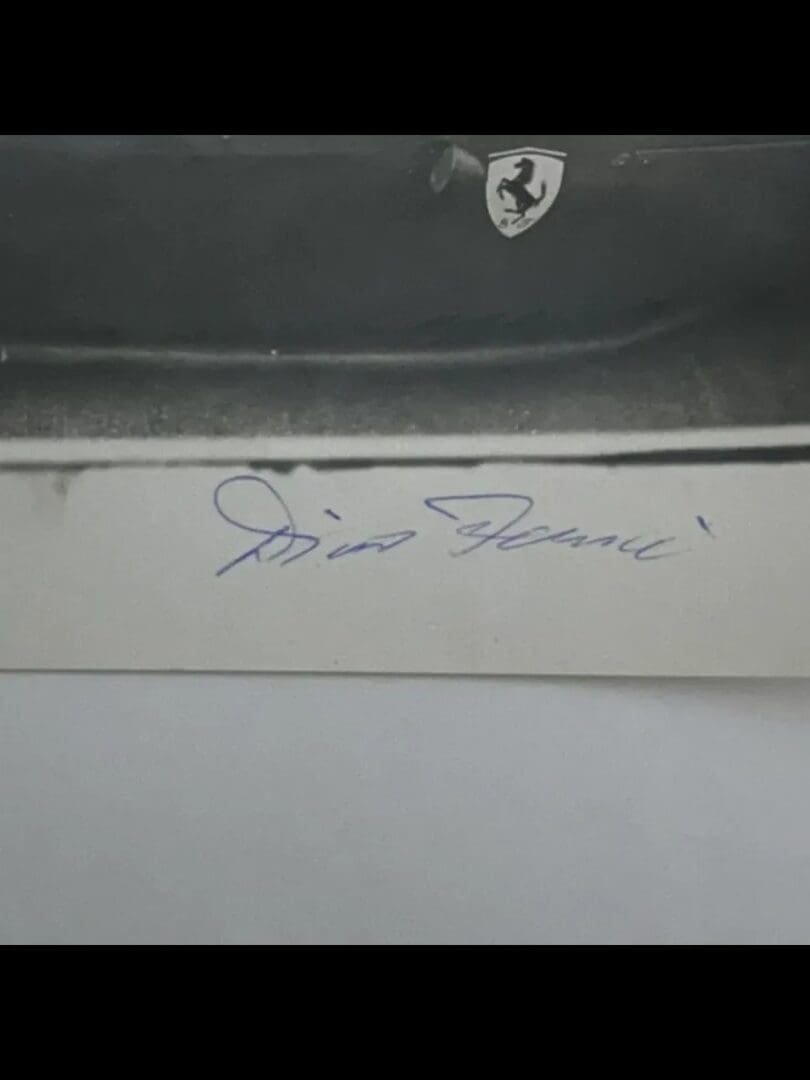 Ferrari emblem and handwritten signature on photo.