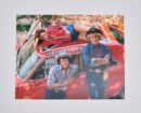 Three people posing on a red car.