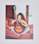Person sitting with guitar on red couch.