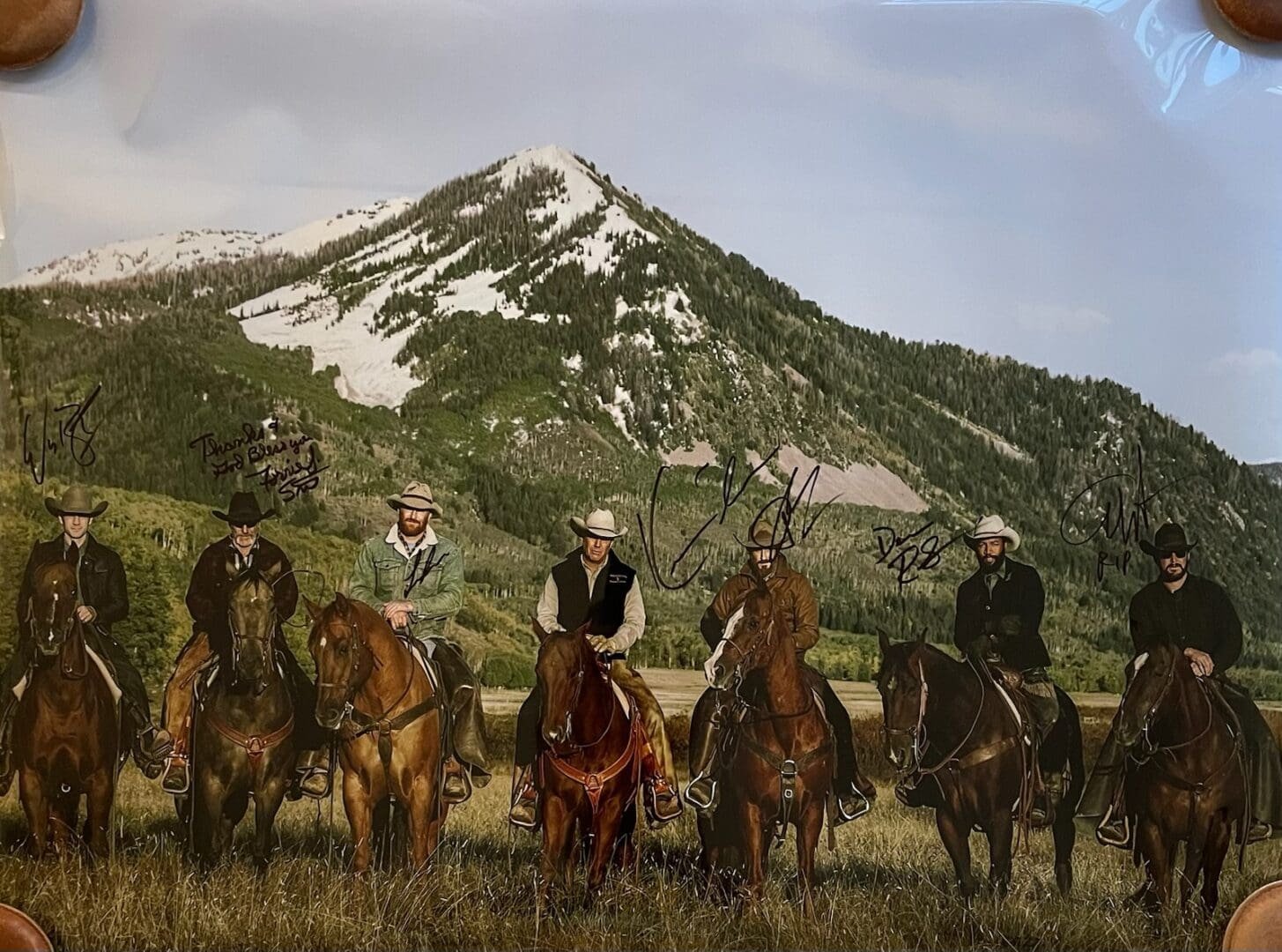 Seven cowboys on horseback before snowy mountain.